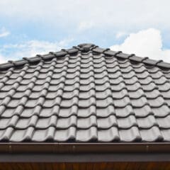 A close-up view of a roof with gray, overlapping ceramic tiles against a partly cloudy sky. The tiles are arranged in a uniform pattern, and the blue sky adds contrast to the structure.